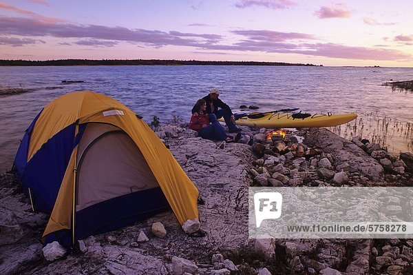 Campers enjoy a campfire next to their kayak  at sunset  on the shore of Lake Huron  Ontario  Canada.