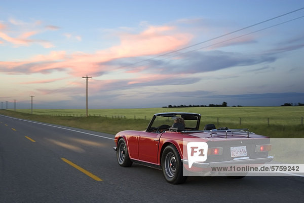 Woman driving red sports car on rural highway  High River  Alberta  Canada.