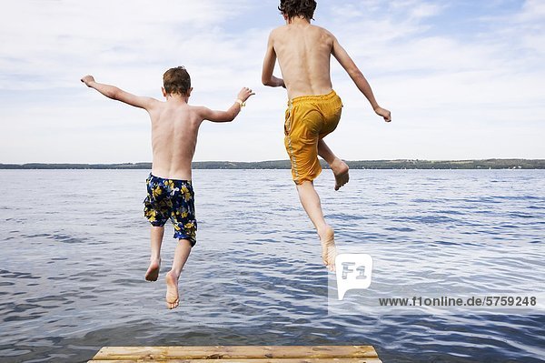 two boys (9 & 12 years old) jumping off dock into lake  Sylvan Lake  Alberta  Canada.