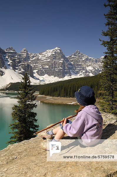 Young girl holding a walking stick and resting while enjoying the view from the rockpile viewpoint at Moraine Lake near Lake Louise  Banff National Park  Alberta  Canada.