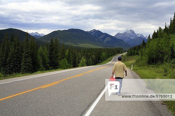 Driver walking with gas can on mountain highway  Kananaskis Provincial Park  Alberta  Canada