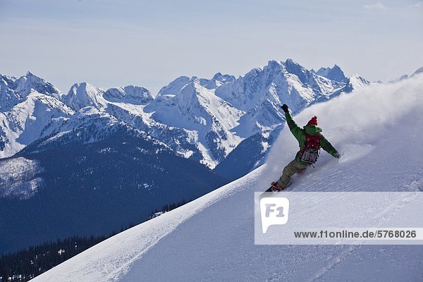 A backcountry snowboarder sprays a powder turn while on a cat ski trip. Monashees  Vernon  Britsh Columbia  Canada