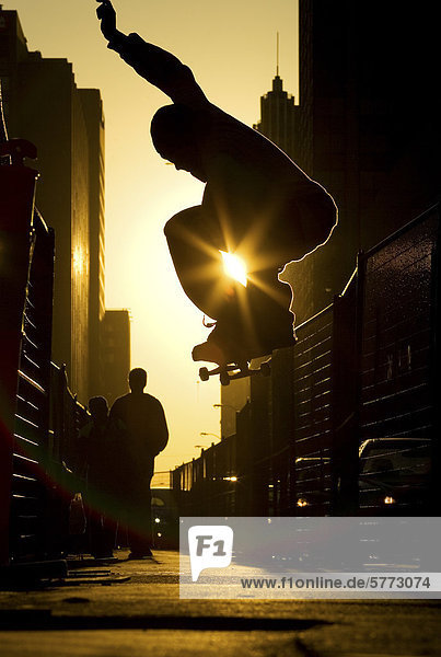 Ein Skateboarder tut ein 'Ollie' entlang einer Straße in der Innenstadt von Toronto bei Sonnenuntergang  Ontario  Kanada.