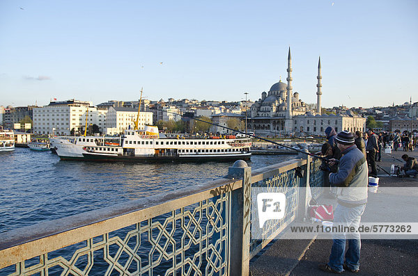 Fishing for sardines on the the Galata Bridge. Yeni Camii  The New Mosque or Mosque of the Valide Sultan located in the Eminönü district of Istanbul  Turkey is in background.