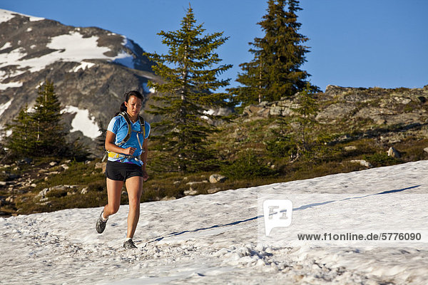 Eine junge asiatische Frau Trailrunning über Schnee in der Trophy Berge  Wells Grey Provincial Park  Clearwater  Britisch-Kolumbien  Kanada