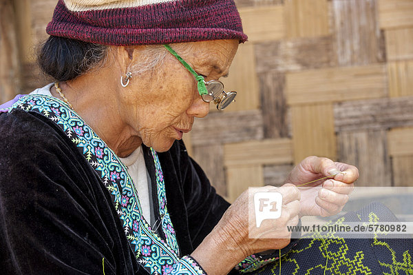 Ältere  traditionell gekleidete Frau mit Brille aus dem Bergstamm oder Bergvolk Schwarze Hmong  ethnische Minderheit aus Ostasien  bei der Handarbeit  Stickerei  Nordthailand  Thailand  Asien