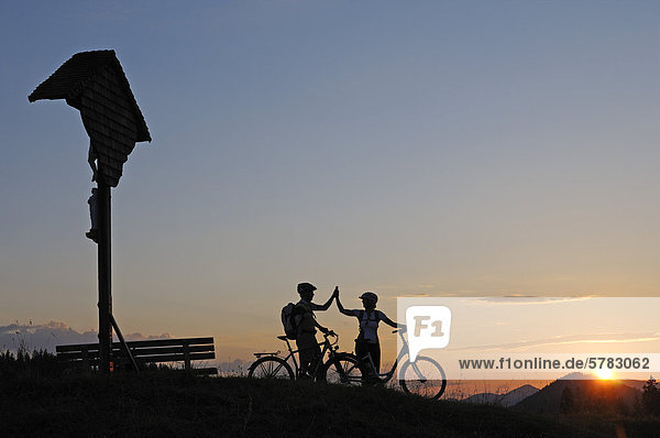 Paar mit Elektrofahrrädern auf der Winklmoos-Alm bei Sonnenuntergang  Reit im Winkl  Chiemgau  Oberbayern  Bayern  Deutschland  Europa