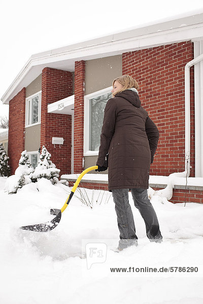 Woman shovelling snow  on her home sidewalk  Winnipeg  Manitoba  Canada