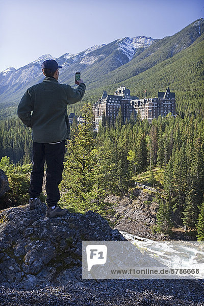 Tourist taking picture of Banff Springs Lodge on smart phone camera.