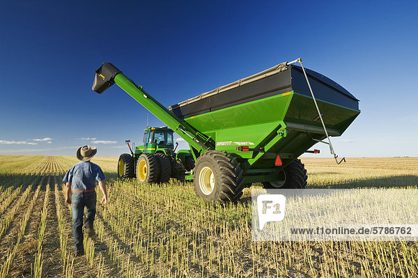 a man next to a tractor and grain wagon during the canola harvest  near Hodgeville  Saskatchewan  Canada