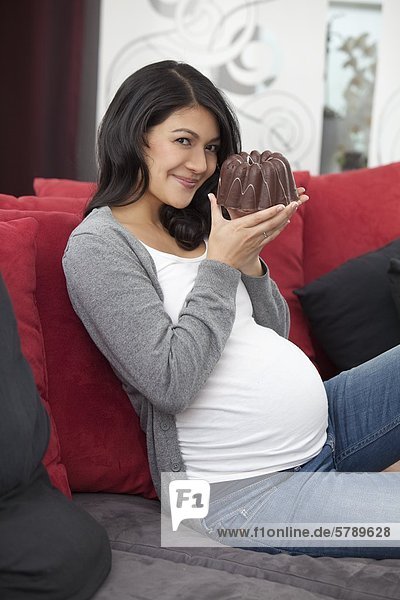 Schwangere Frau mit einem Kuchen auf der Couch