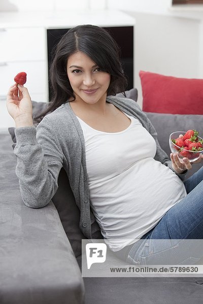 Schwangere Frau auf der Couch isst Erdbeeren