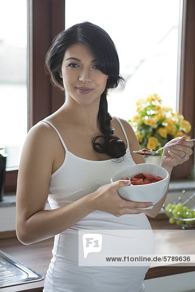 Schwangere Frau isst Erdbeeren aus einer Schale