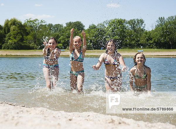 Four girls in bikinis splashing in bathing lake