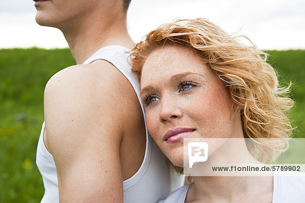 Young woman leaning against back of her boyfriend outdoors