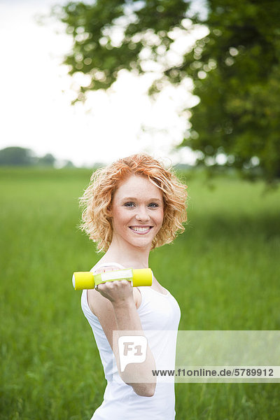 Lächelnde junge Frau trainiert mit Handhantel im Freien