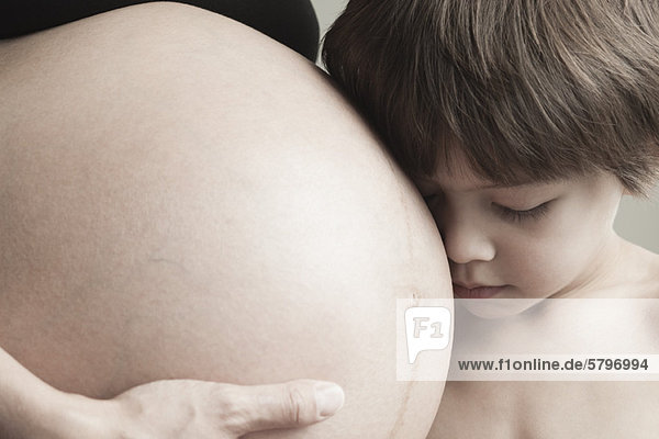 Junge ruht Kopf auf dem schwangeren Bauch der Mutter  abgeschnitten