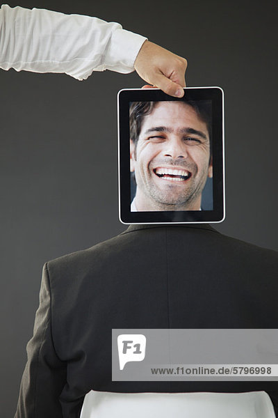Mann versteckt hinter digitalem Tablett mit Bild des lachenden Mannes  Rückansicht