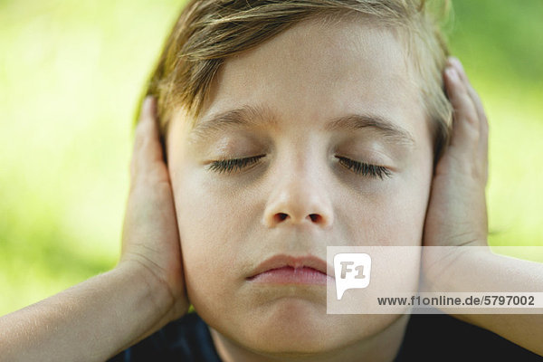 Junge  der die Ohren mit den Händen bedeckt  die Augen geschlossen.