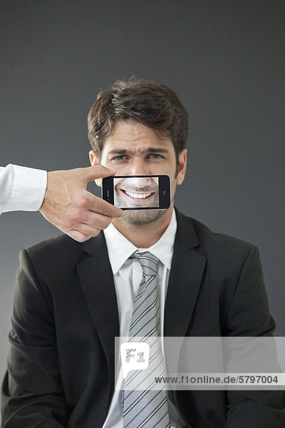 Man with mouth concealed behind smartphone displaying image of his own smile