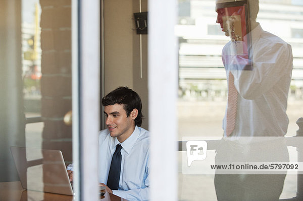 Businessman in office seen from outside of window  reflection of man using cell phone outdoors