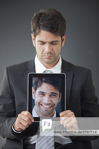 Mann  der ein digitales Tablett hochhält  das ein Bild von sich selbst zeigt.