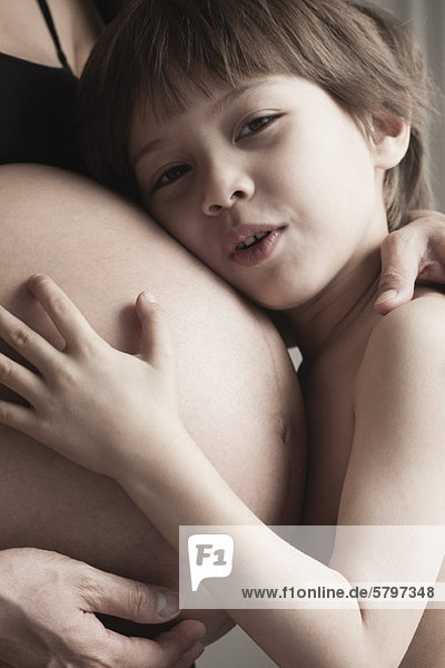 Junge  der den schwangeren Bauch der Mutter umarmt.