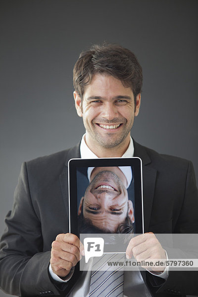Mann  der ein digitales Tablett hochhält  das ein auf dem Kopf stehendes Bild von sich selbst zeigt.
