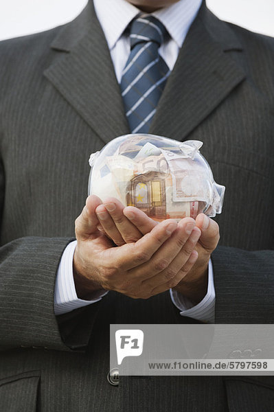 Mann mit transparentem Sparschwein gefüllt mit Euro  beschnitten