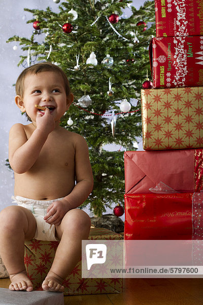 Baby-Mädchen isst Snack neben hohem Stapel Weihnachtsgeschenke