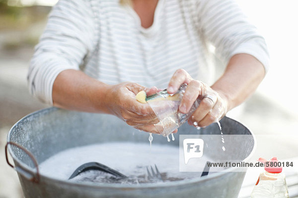 Frau wäscht Glas in seifenwassergefülltem Behälter