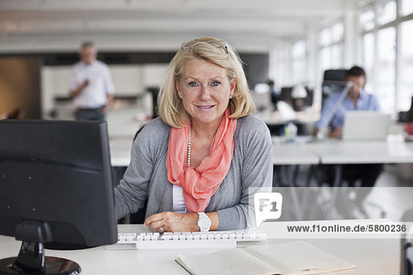 Portrait of a smiling business woman sitting in office with colleagues in background