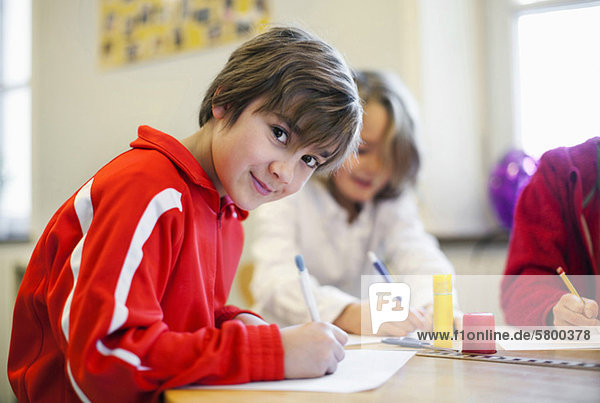 Portrait of smiling boy studying with friends in the background
