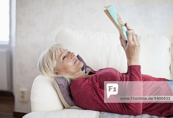 Reife Frau  die auf dem Sofa ein Buch liest.