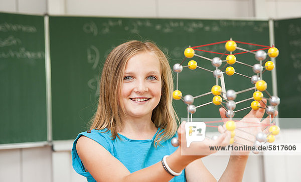 Lächelnde Schülerin hält ein Molekular-Modell im Klassenzimmer  Portrait