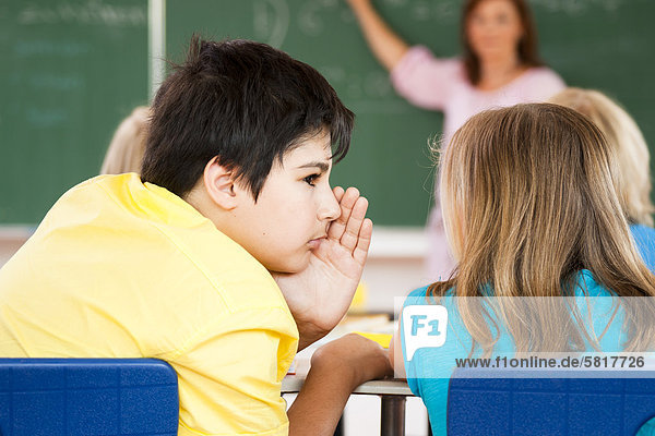 Junge flüstert mit einem Mädchen im Klassenzimmer