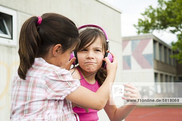 Zwei Mädchen mit Kopfhörern auf dem Schulhof