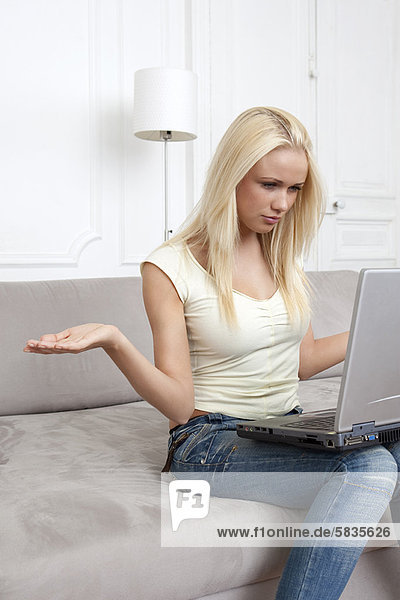 Woman shrugging at laptop on couch