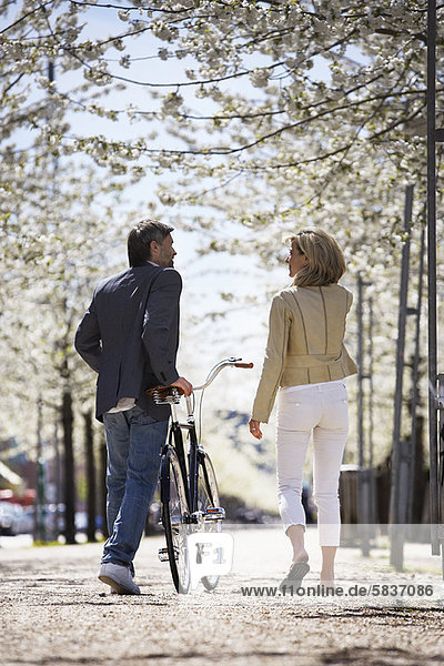 Couple walking bicycle in park
