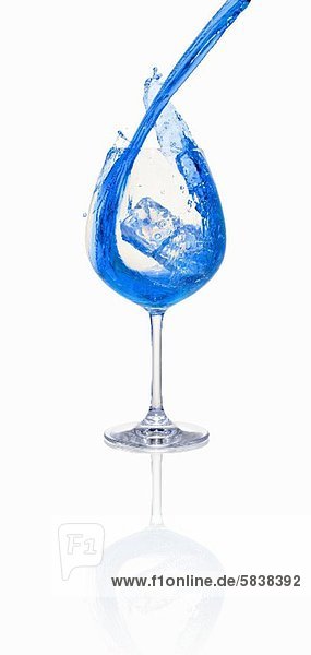 Blauen Cocktail in ein Glas mit Eiswürfeln einschenken