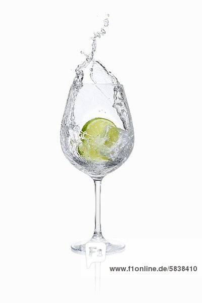Limettenscheibe fällt in ein Wasserglas