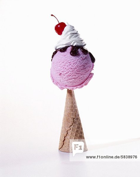 'Scoop of Raspberry Ice Cream with Chocolate Sauce  Whipped Cream and a Cherry on an Upside Down Cone