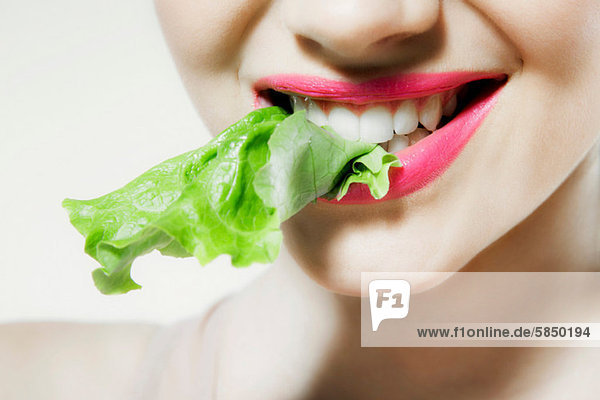 Junge Frau beißt Kopfsalat  Mund