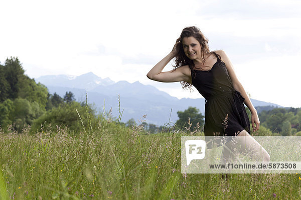 Junge Frau posiert mit kurzem schwarzem Kleid in hohem Gras