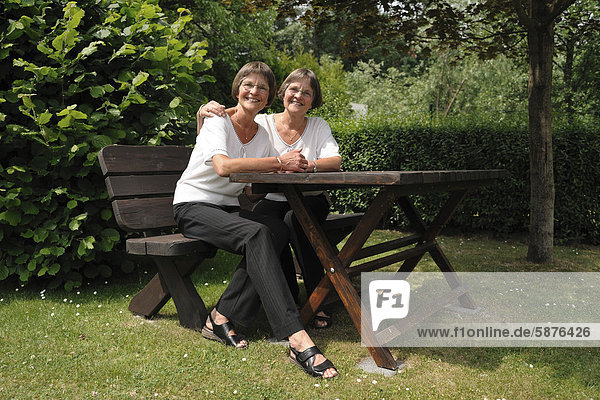 Zwei rüstige Zwillingsschwestern sitzen auf einer Gartenbank