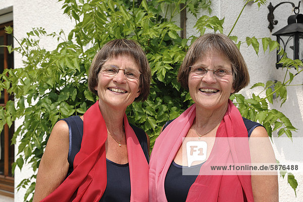 Zwei rüstige Zwillingsschwestern  gleich gekleidet mit roten Schals  Portrait