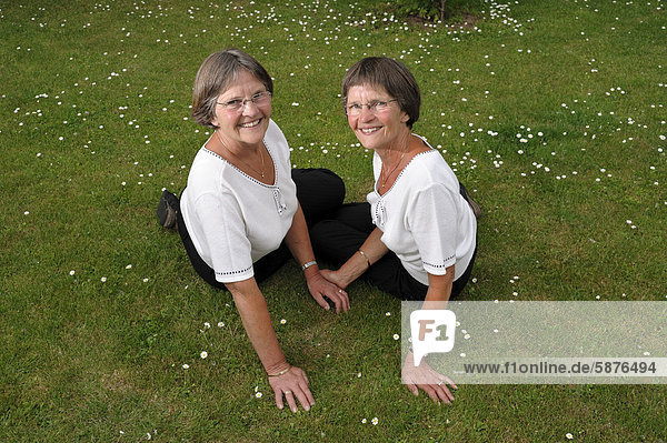 Zwei rüstige Zwillingsschwestern sitzen auf einer Wiese