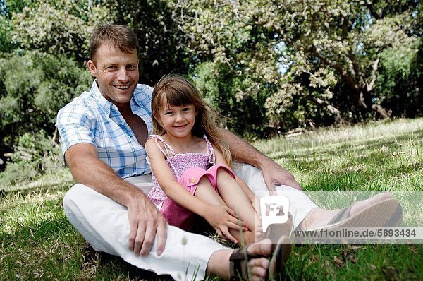 Portrait of a girl sitting with her father in a garden and smiling