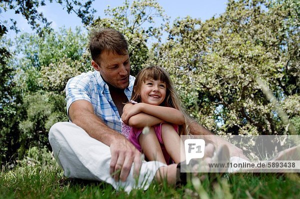 Close_up of a girl sitting with her father in a garden and smiling