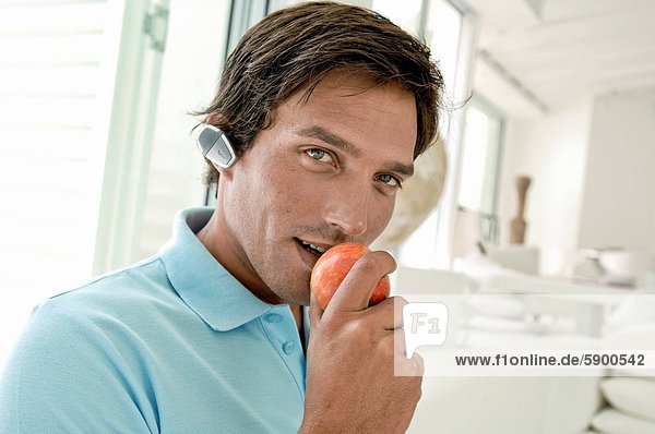 Portrait of a mid adult man wearing a hands free device and eating an apple